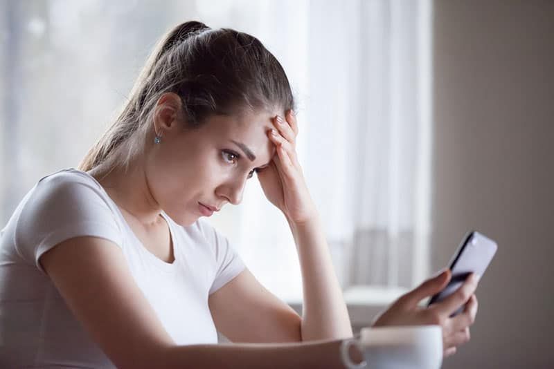 besorgte Frau, die auf das Telefon schaut