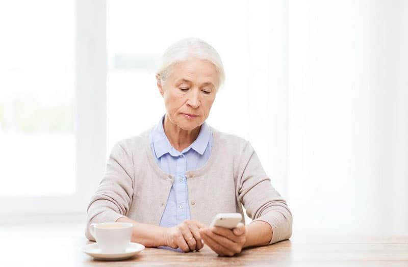 dona gran marcant amb un telèfon intel·ligent mentre està asseguda amb una tassa a la taula