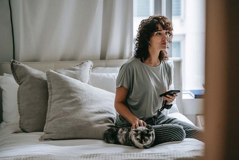peinzende vrouw die smartphone vasthoudt terwijl ze op het bed zit