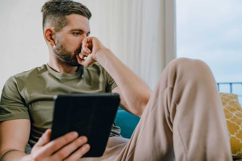 een droevige peinzende man met een tablet die thuis op de bank zit