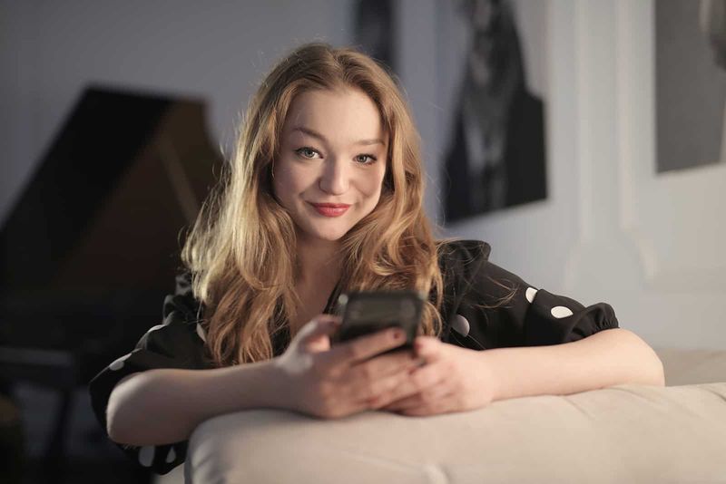 lachende vrouw die smartphone vasthoudt terwijl ze op de bank zit