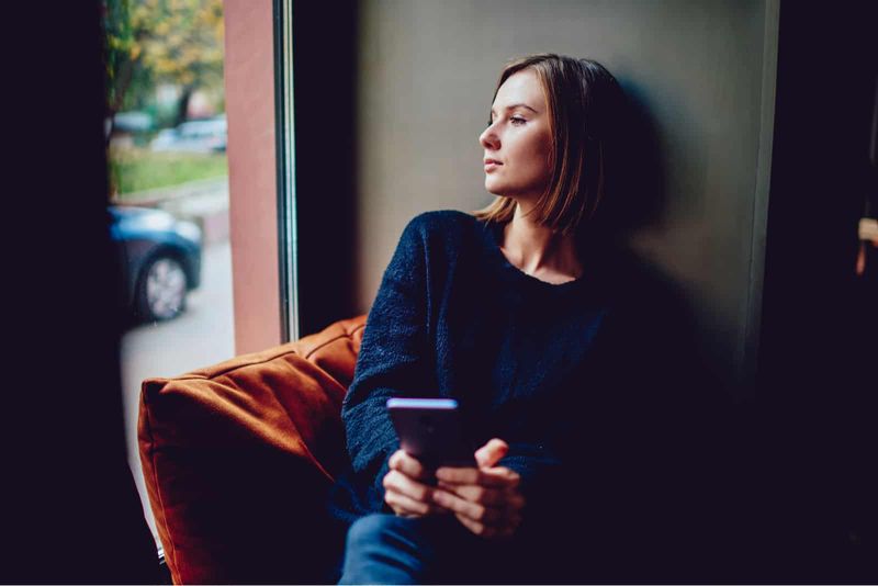 Nadenkende jonge vrouw die haar smartphone vasthoudt