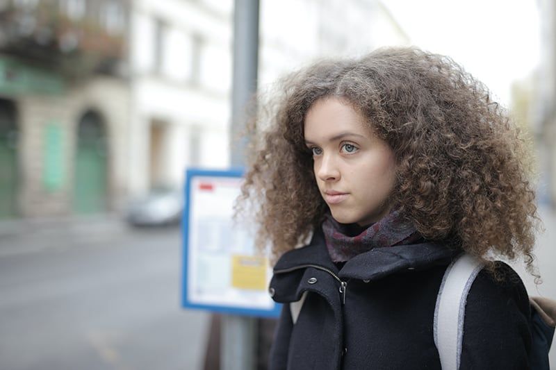 zamišljena žena koja stoji na ulici i gleda u stranu