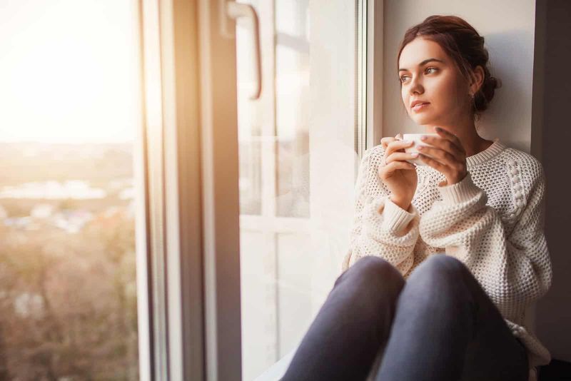 Frau sitzt am Fenster und trinkt Tee