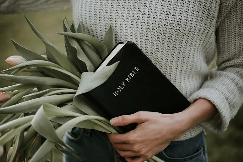 frau, die eine heilige bibel und einen blumenstrauß hält