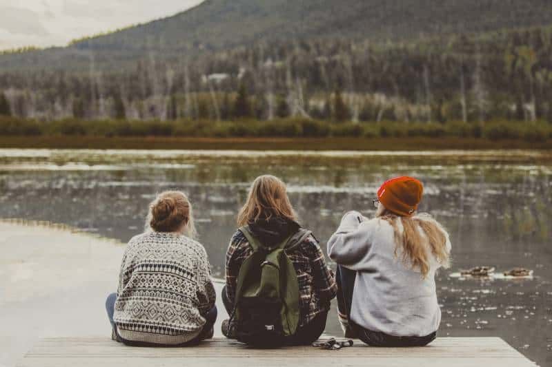 tri prijateljice sjede uz jezero