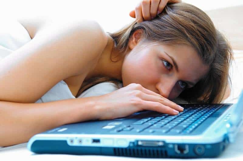 djevojka koja leži u krevetu i tipka na laptopu