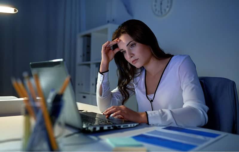 امرأة تواجه الكمبيوتر المحمول بينما تفكر بعمق داخل إعداد المكتب