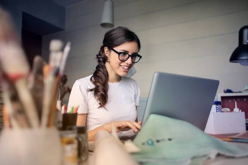 lächelnde Frau mit ihrem Laptop mit Tisch voller Sachen