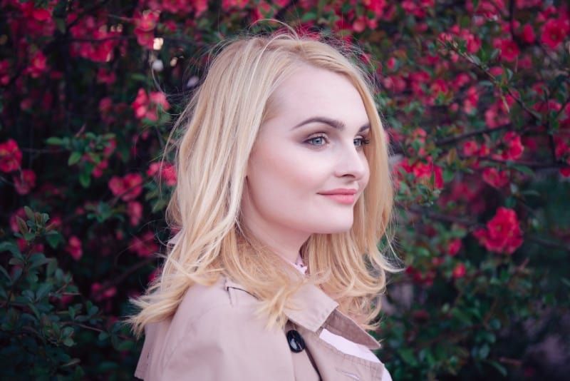 mulher loira em pé perto de flores vermelhas