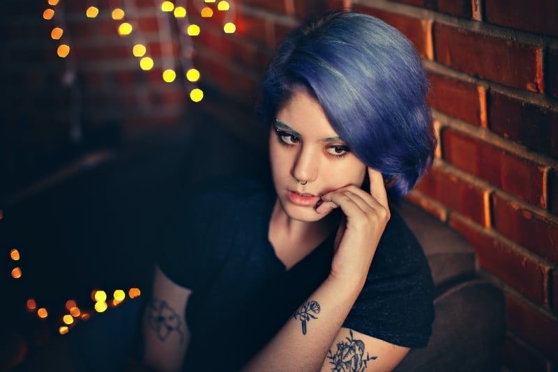 mulher tatuada com cabelo azul sentada perto da parede