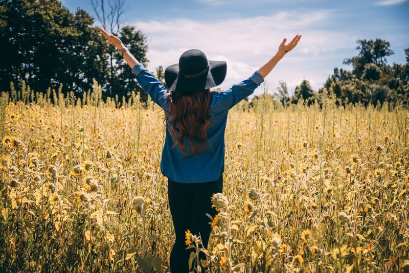 wanita mengangkat kedua tangan sambil berdiri di ladang bunga matahari