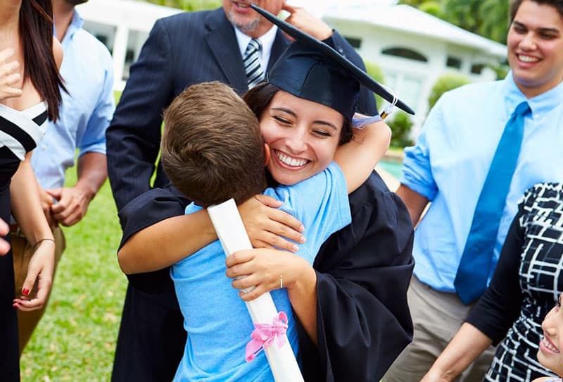 orgullós germà petit abraçant una dona amb un vestit de graduació amb gent al seu voltant