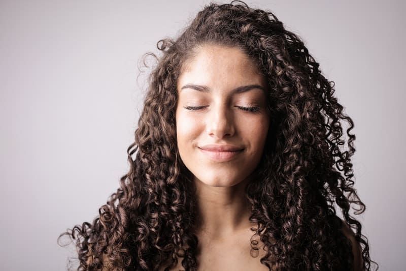 Porträtfoto einer lächelnden Frau mit lockigem Haar, während sie ihre Augen schließt