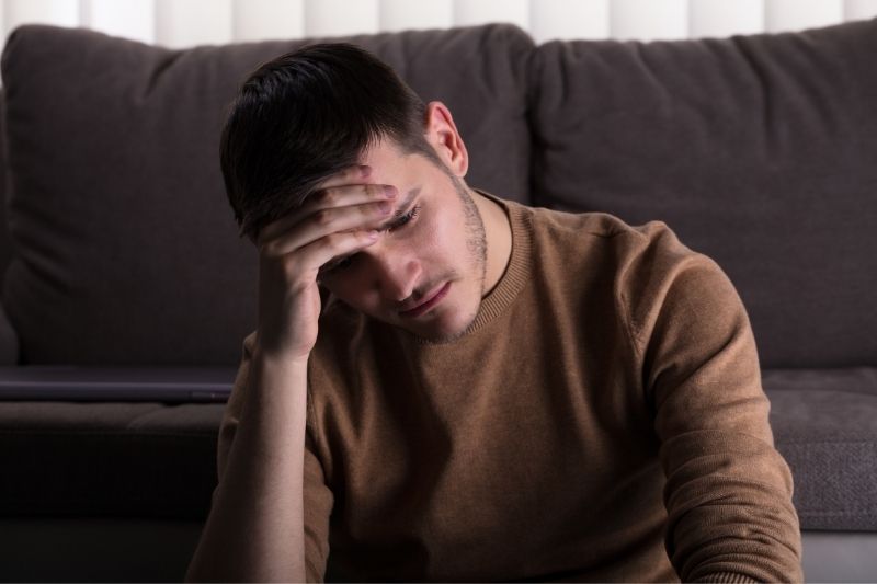 om trist care stă în fața canapelei din sufragerie