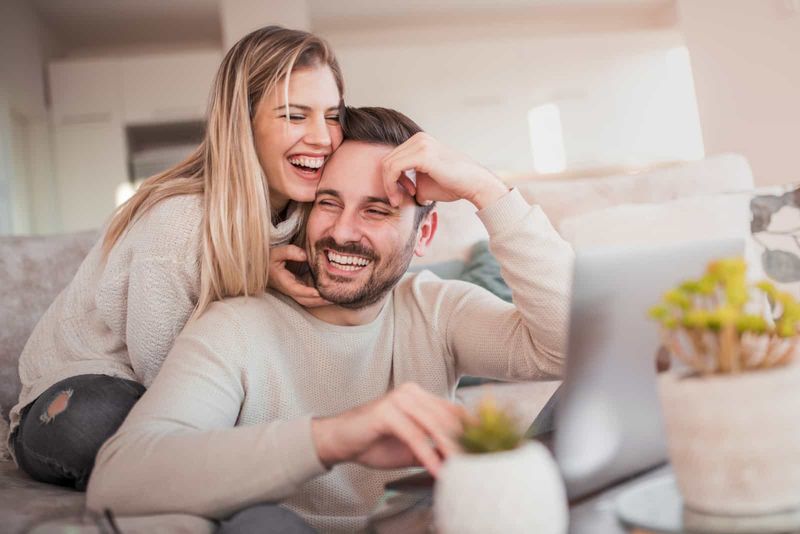 رجل يجلس خلف جهاز كمبيوتر محمول امرأة تحضنه وتضحك