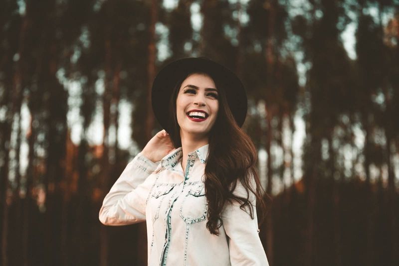 phụ nữ với mũ đen mỉm cười trong khi đứng trong rừng