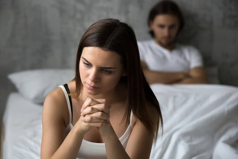 triste mulher sentada na cama na frente de seu homem