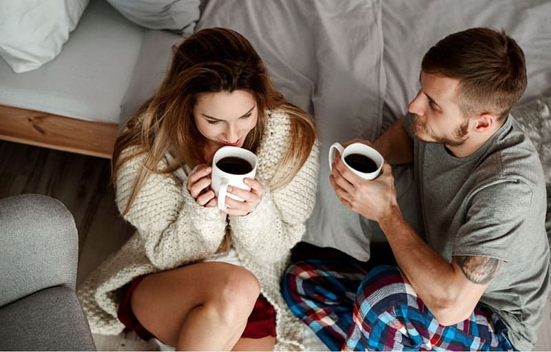 paar met koffie in de slaapkamer zittend op de vloer bij het bed