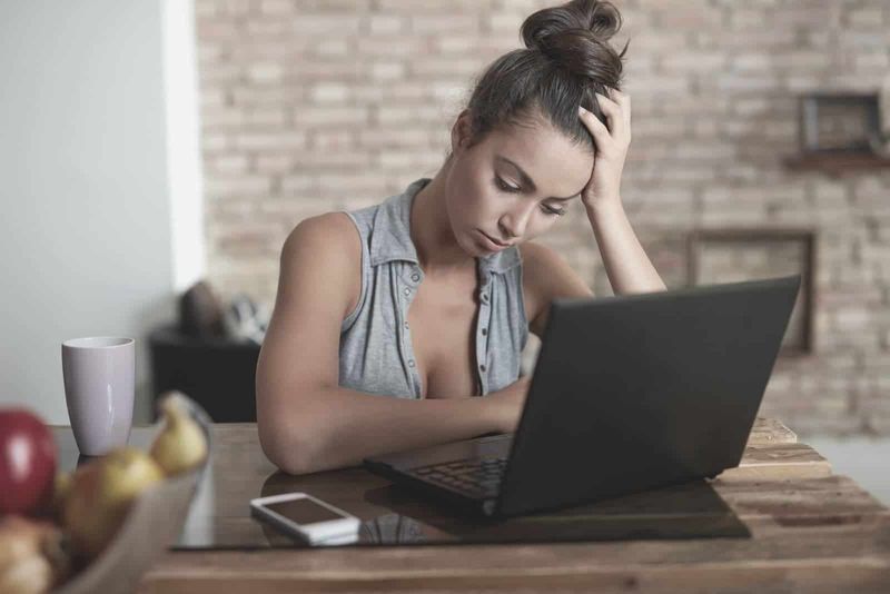 malungkot na babae na gumagamit ng laptop sa loob ng silid-kainan