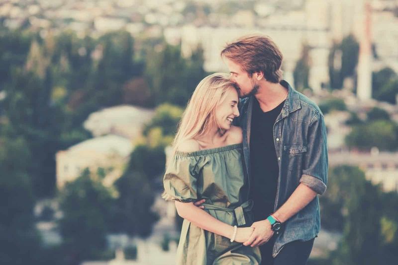 cặp đôi trẻ đang đi bộ trên đường trong khi người đàn ông hôn người phụ nữ