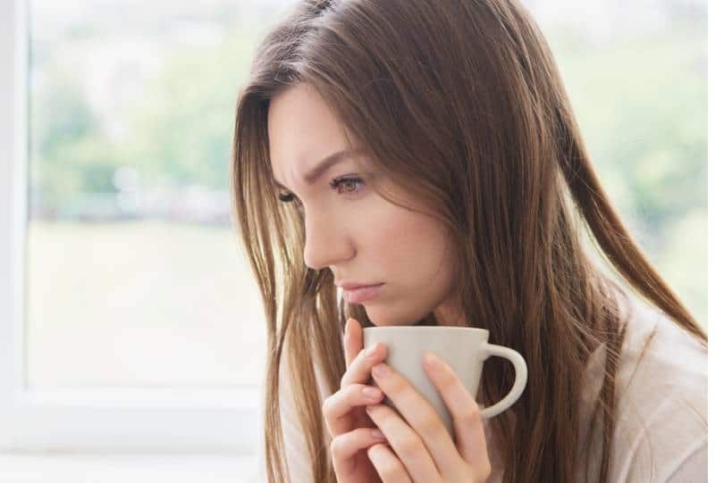 traurige frau, die tasse hält und zu hause denkt