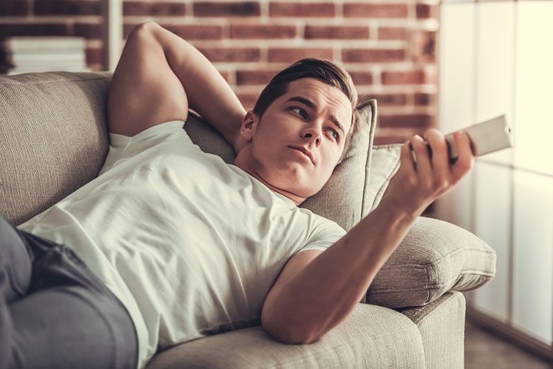 mężczyzna leżący na kanapie i oglądający telewizję