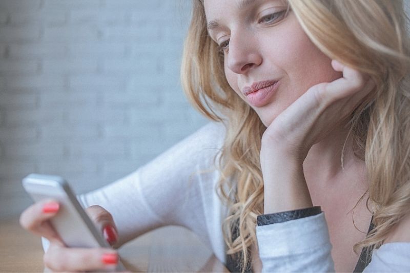 млада замислена жена изпраща съобщения на смартфона си, докато с една ръка поддържа брадичката си