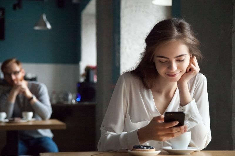 жена, която чете текстово съобщение на смартфона си в кафенето със замъглен фон