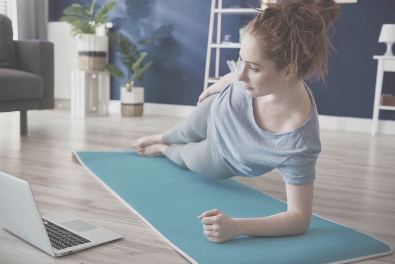 junge Frau, die auf der Matte trainiert, während sie zu Hause ein Video auf dem Laptop ansieht