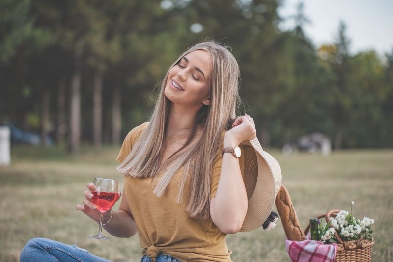 Nasmejana ženska na pikniku v parku, ki se dobro zabava z vinom