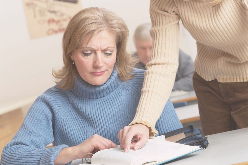 Reife Frau lernt und unterrichtet von einem Lehrer in einem Raum mit einem alten Mann, der im Hintergrund lernt