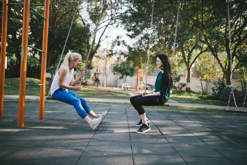 dua wanita tersenyum duduk di ayunan di taman