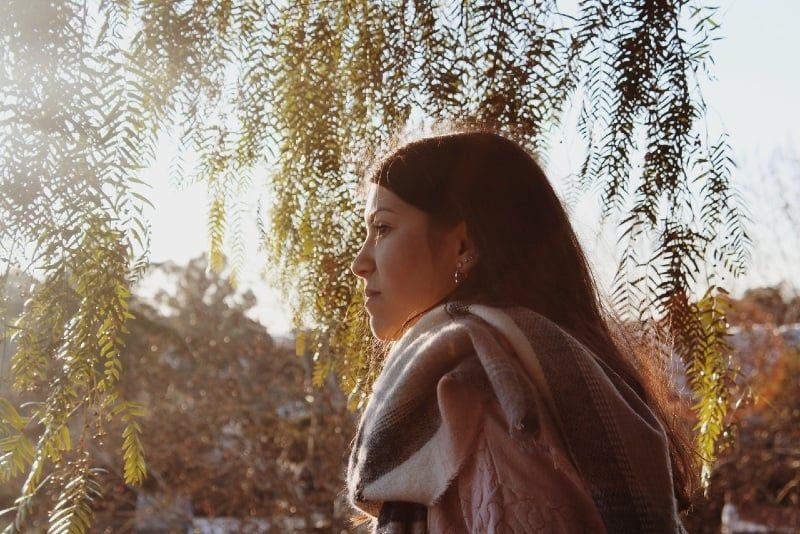 wanita dengan syal berdiri di dekat pohon