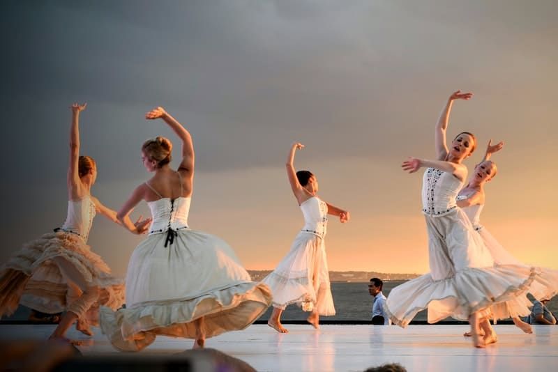 5 femei în rochie albă dansând sub cerul gri în timpul apusului