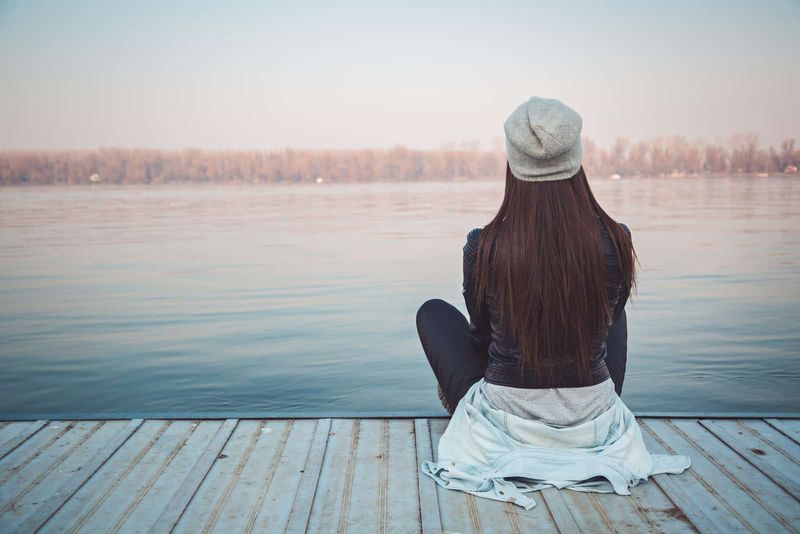 một người phụ nữ với chiếc mũ trên đầu ngồi trên bến tàu