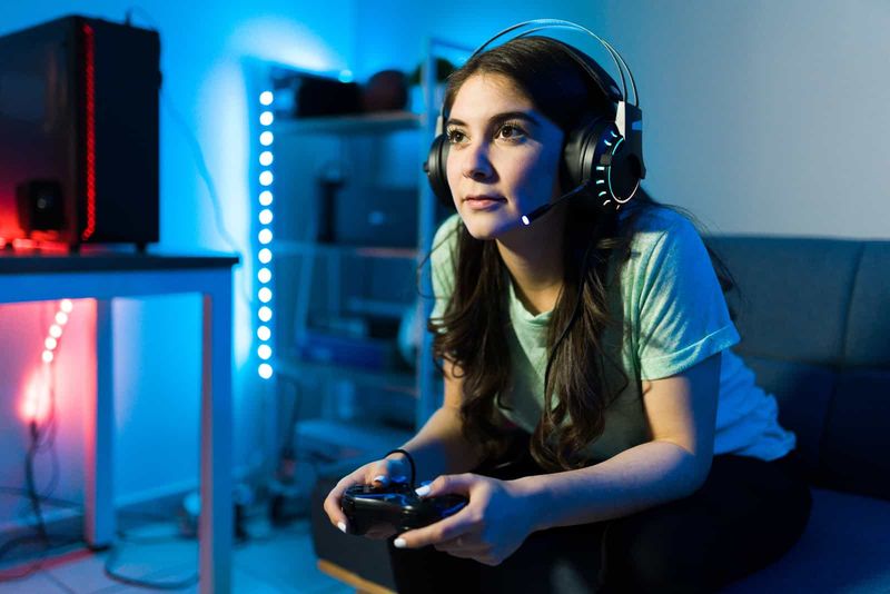 uma mulher sentada em um sofá com fones de ouvido e jogando videogame