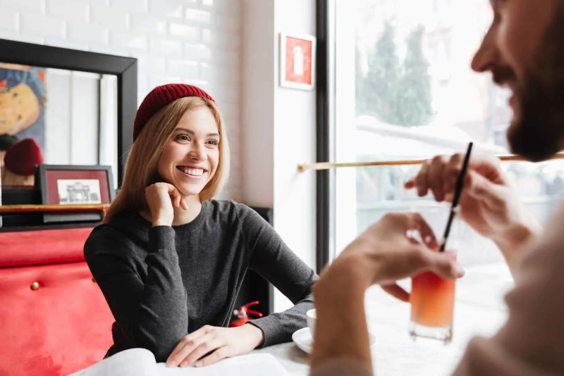   Lächelnde Blondine im Gespräch mit bärtigem Mann im Café