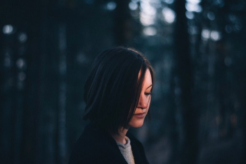vrouw in zwarte jas staande in het bos