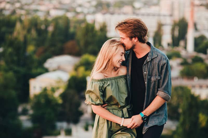 casal sorridente homem beija mulher na testa do lado de fora