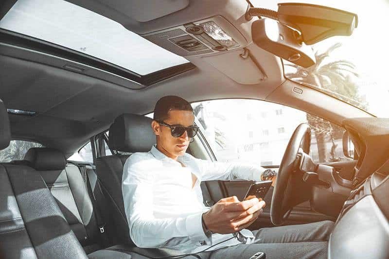 homem de óculos escuros e camisa azul digitando em seu telefone