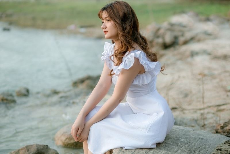 Frau im weißen Kleid auf Stein sitzend