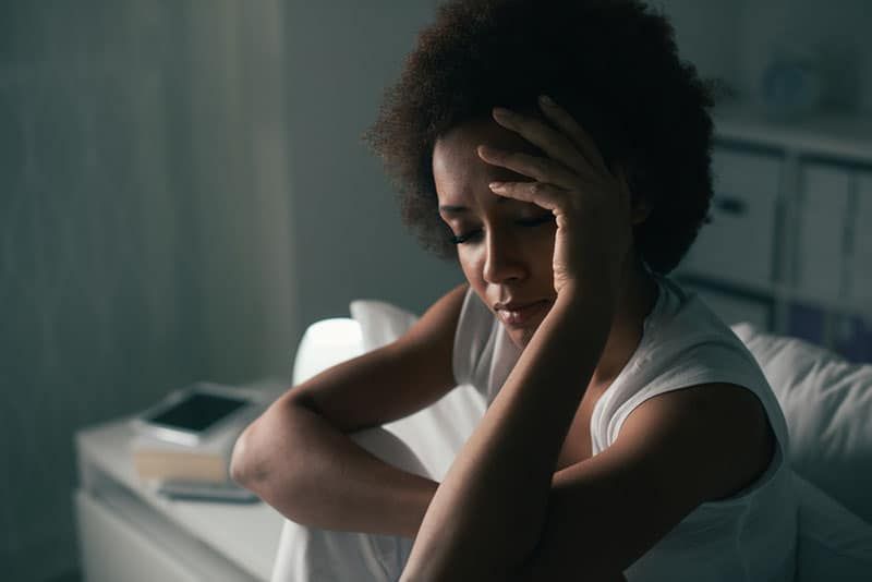 Wanita depresi yang sedih menderita insomnia, dia duduk di tempat tidur dan menyentuh dahinya, gangguan tidur dan konsep stres
