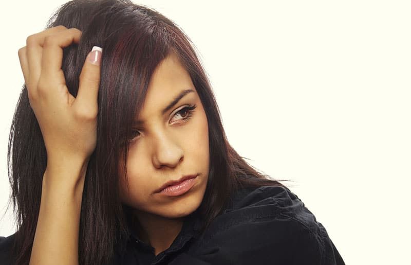 Wanita muda dengan ekspresi serius bersandar dengan tangan di rambut.