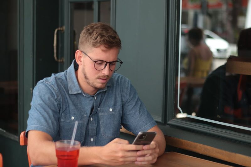 мужчина в очках с помощью смартфона, сидя за столом
