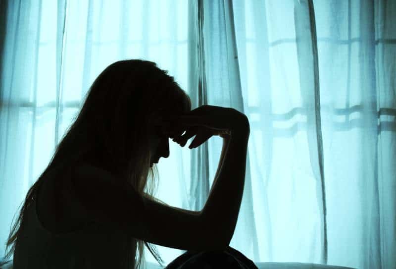 besorgte frau, die am fenster im bett sitzt