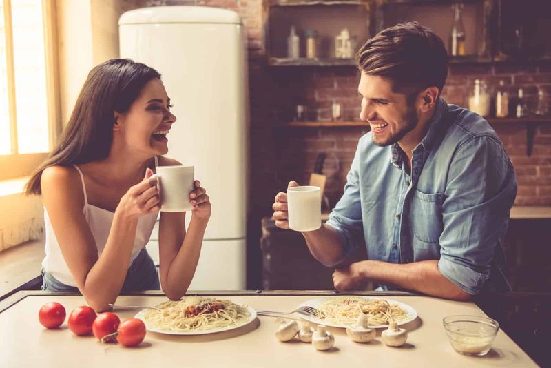 nakangiting lalaki at babae na nakaupo sa kusina na nag-uusap