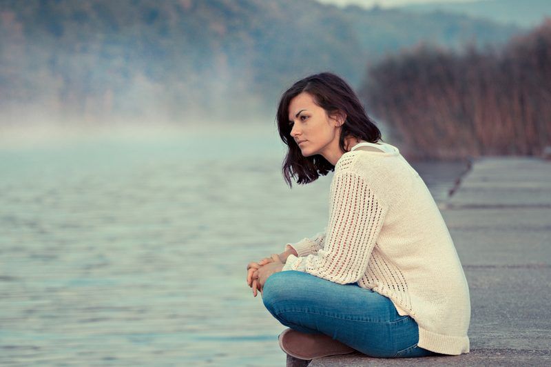 Eine Frau sitzt am Fluss auf einem Pier