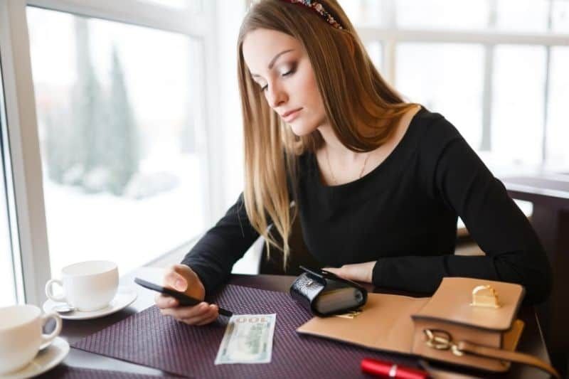 kobieta czeka na SMS-a lub telefon ze smartfona siedząca przy stole w pomieszczeniu