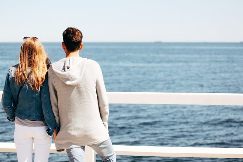 homem e mulher de mãos dadas e olhando para o mar